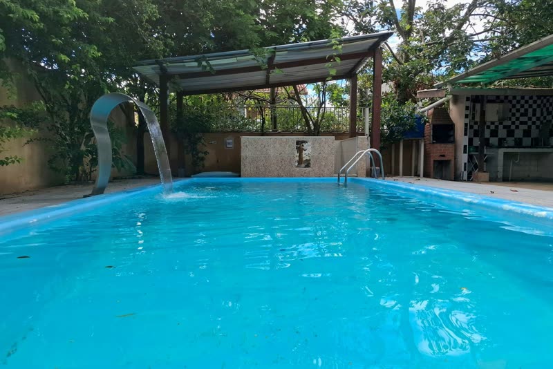 Pool at Casarão do Indaiá with a waterfall and a brick barbecue in the background